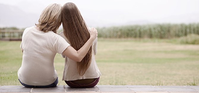 actor portrayal of two women leaning on each other looking at field