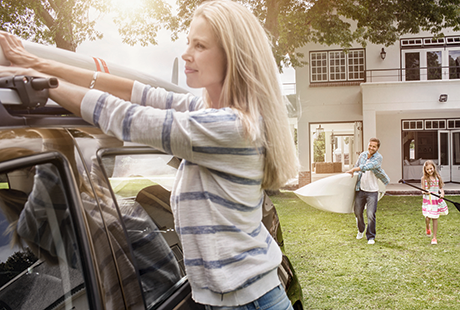 actor portrayal of woman tying a kayak on the roof of the car while a man holds a kayak and little girl holds a paddle